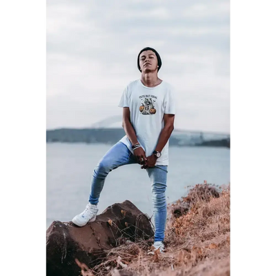 Model wearing a Cute But Feral unisex tee with raccoon and pumpkin design, standing by a lake.