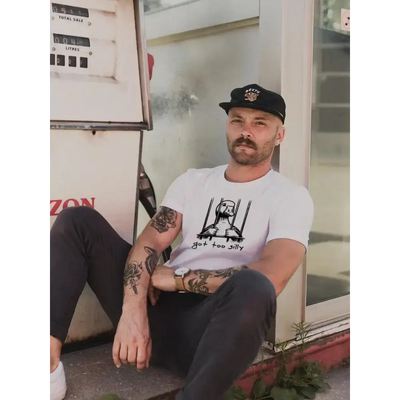 Man sitting by a gas station wearing a 'Got Too Silly' unisex tee, showcasing comfort and style.